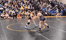 two women are wrestling on a wrestling mat in front of a crowd of people .