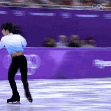 a blurry picture of a person ice skating in front of a purple wall with the olympic rings on it