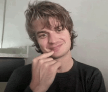 a young man in a black shirt is making a funny face with his finger on his chin .