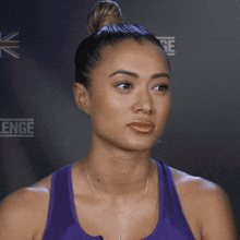 a woman in a purple tank top is making a funny face in front of a wall that says challenge