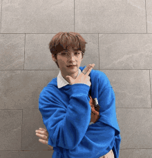 a young man wearing glasses and a blue sweater stands in front of a wall