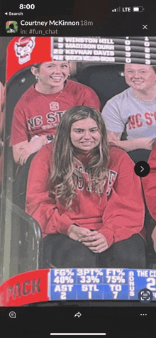 a woman in a red shirt with nc state on it sits in the stands