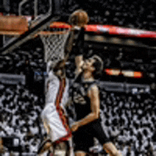 two basketball players are playing a game of basketball and one of them is jumping to dunk the ball .