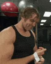 a man in a black tank top is wrapping his hands in a gym with a red ball in the background .