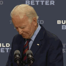 a man in a suit and tie stands in front of two microphones with the word better on the back