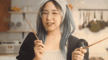 a woman with blue hair and glasses is holding a pair of chopsticks .