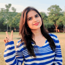 a woman in a blue and white striped sweater giving the peace sign