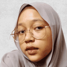 a woman wearing glasses and a gray hijab looks at the camera