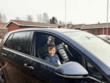 a young boy is sitting in the driver 's seat of a black car