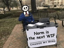 a man is sitting at a table with a sign that says `` norm is the next wif '' .