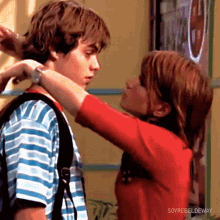 a girl in a red shirt is touching a boy 's neck .