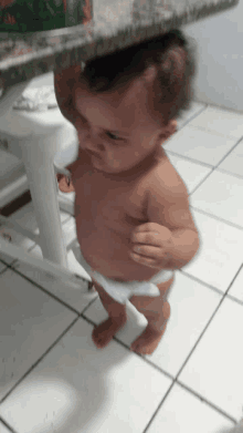 a baby in a diaper is standing in front of a table