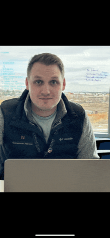 a man wearing a columbia vest sits in front of a laptop computer