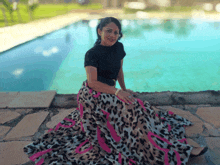 a woman wearing a leopard print skirt sits on the edge of a pool