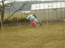 a woman in a blue jacket and pink pants is walking in a field with a bird feeder in the background