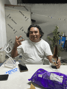 a man sits at a table holding a bottle of beer and a bag of chips