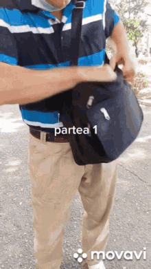 a man in a blue and white striped shirt is holding a black bag with partea 1 written on the bottom