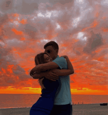 a man and woman hugging on a beach with a sunset in the background