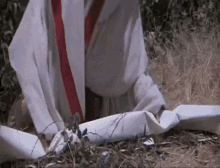 a man in a white robe and red tie is sitting on the ground with a piece of paper .