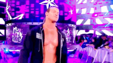 a shirtless wrestler is standing in front of a purple wall that says rock your world .