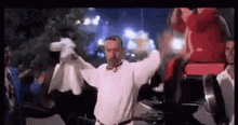 a man in a white shirt is dancing with his arms outstretched in front of a crowd of people .