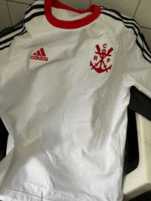 a white adidas shirt with red stripes and an anchor on it