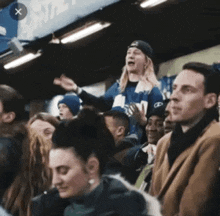 a group of people are sitting in a stadium watching a game and a woman is standing in the stands .