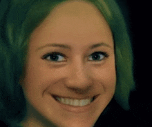 a close up of a woman 's face with green hair smiling and looking at the camera .