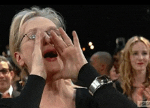 a woman wearing glasses is covering her face with her hands in a crowd .