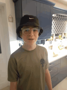 a young boy wearing a nike hat and glasses stands in a kitchen