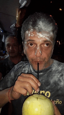 a man with white paint on his face drinks from a coconut with a straw