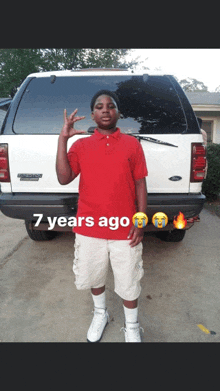 a young man in a red shirt is standing in front of a white ford expedition