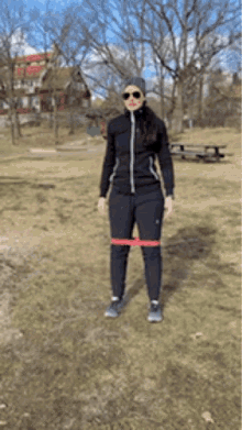 a woman wearing sunglasses and a hat is standing in a field with a resistance band around her waist .