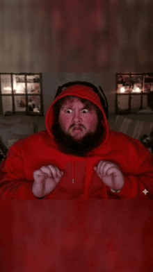 a bearded man in a red hoodie is sitting at a table