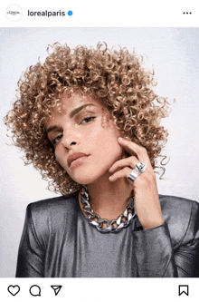 a woman with curly hair is wearing a silver necklace