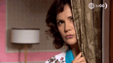 a woman peeking out from behind a curtain with tvgo written on the bottom right