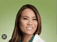 a woman in a white lab coat smiles with a green background behind her