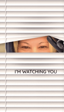 a woman peeking through blinds with the words " i 'm watching you " on the bottom