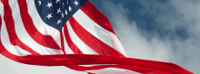 an american flag is waving in the wind against a cloudy blue sky