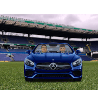 two men are sitting in a blue mercedes on the grass