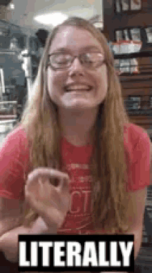 a woman wearing glasses and a red shirt is sitting at a table with a sign that says literally on it .