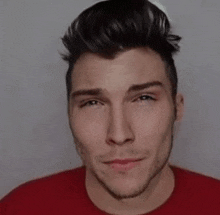 a young man wearing a red t-shirt and a white hat is looking at the camera .