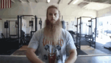 a man with a long beard is standing in a gym wearing a t-shirt with a picture of a deer