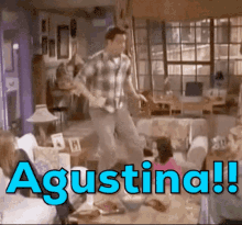 a man in a plaid shirt is dancing in a living room with the word agustina written in blue letters .