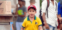 a young boy wearing a yellow shirt and a red hat stands in front of a box that says 2 bottles