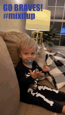 a baby with a pacifier in his mouth is sitting on a couch with a sign that says go braves