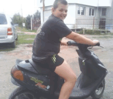 a young boy is riding a black scooter down a dirt road .