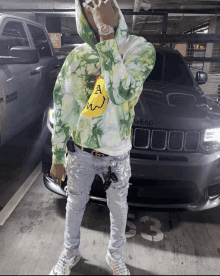 a man wearing a green tie dye hoodie stands in front of a jeep