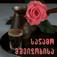 a pink rose sits next to a cup of coffee and a pitcher