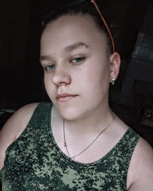 a young woman wearing a camouflage tank top and a necklace